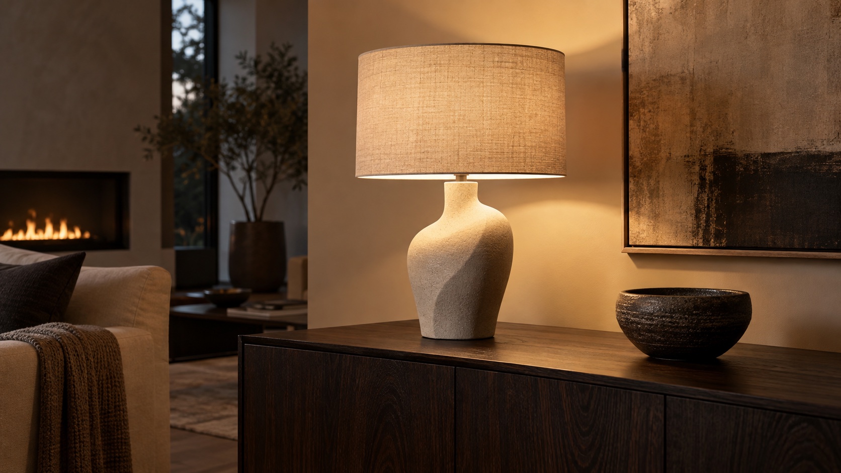 Sculptural ceramic lamp casting a warm glow over a dark wooden credenza.